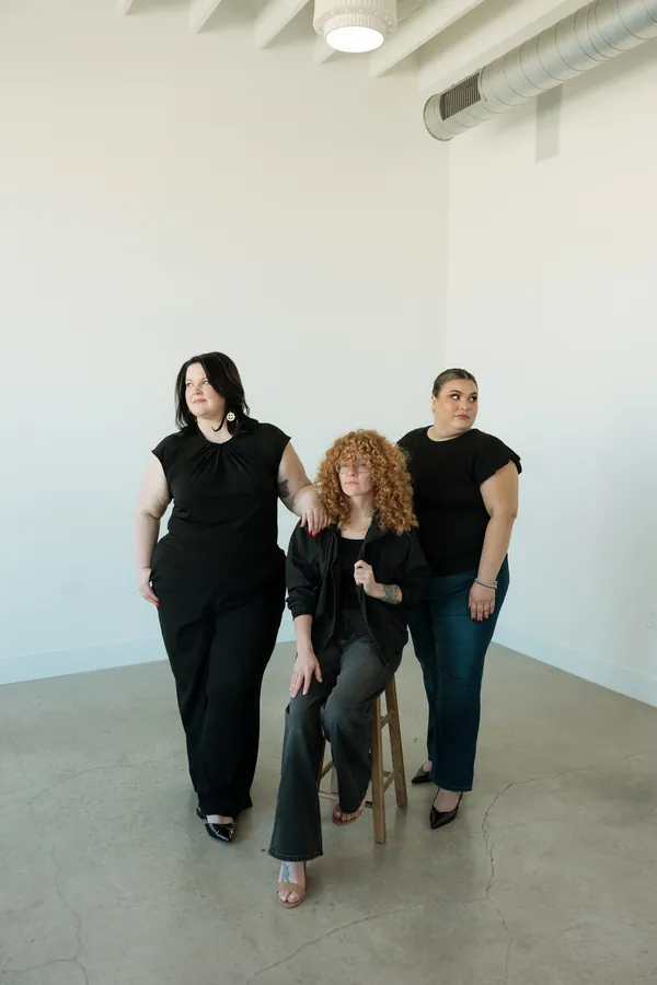 Three stylists posing together, one seated on a stool