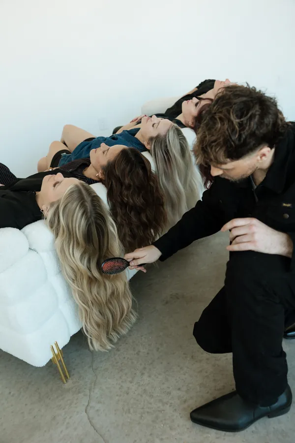 Stylist brushing out hair hanging over the edge of a white sofa